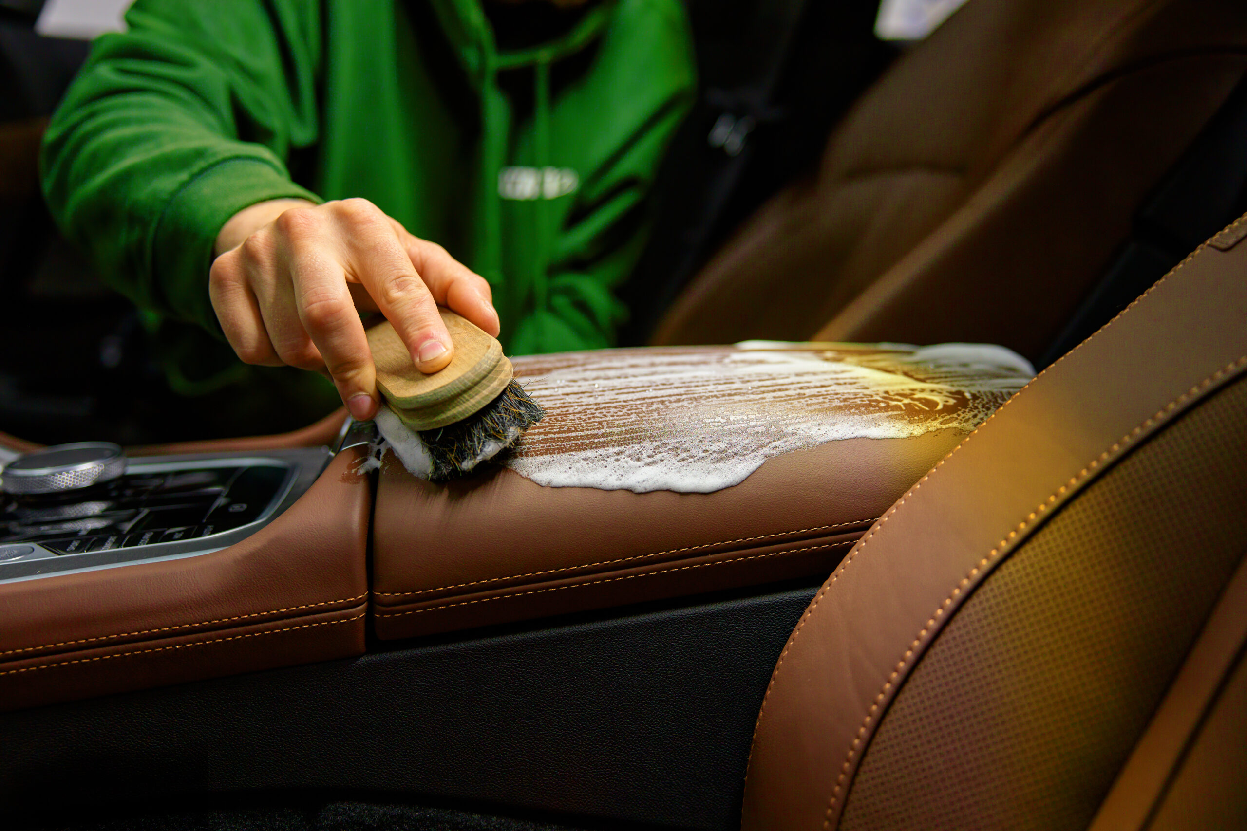 closeup leather car interior cleaning with foam detergent and brush